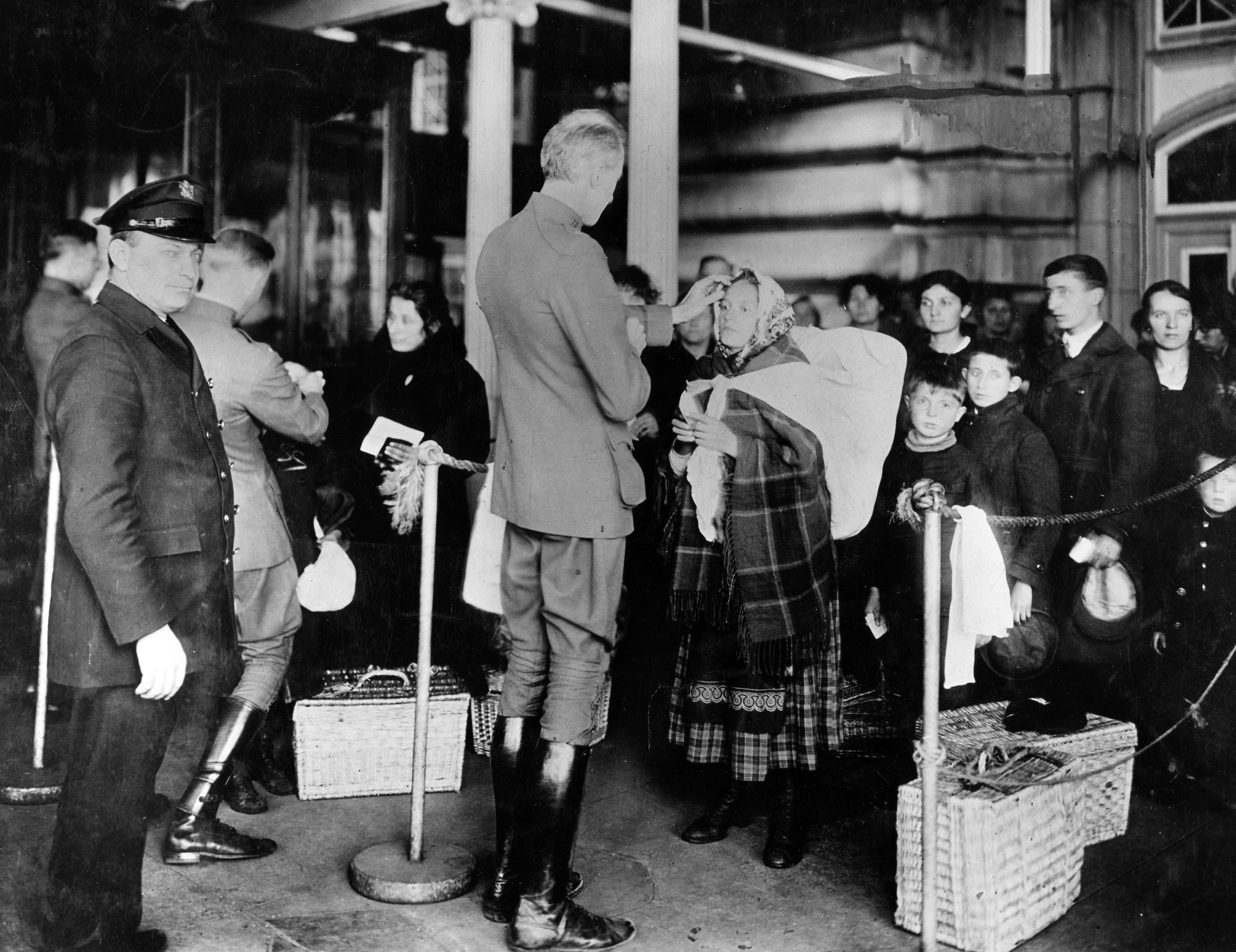 A line of people are shown with the person at the front being examined by a member of the Public Health Service.