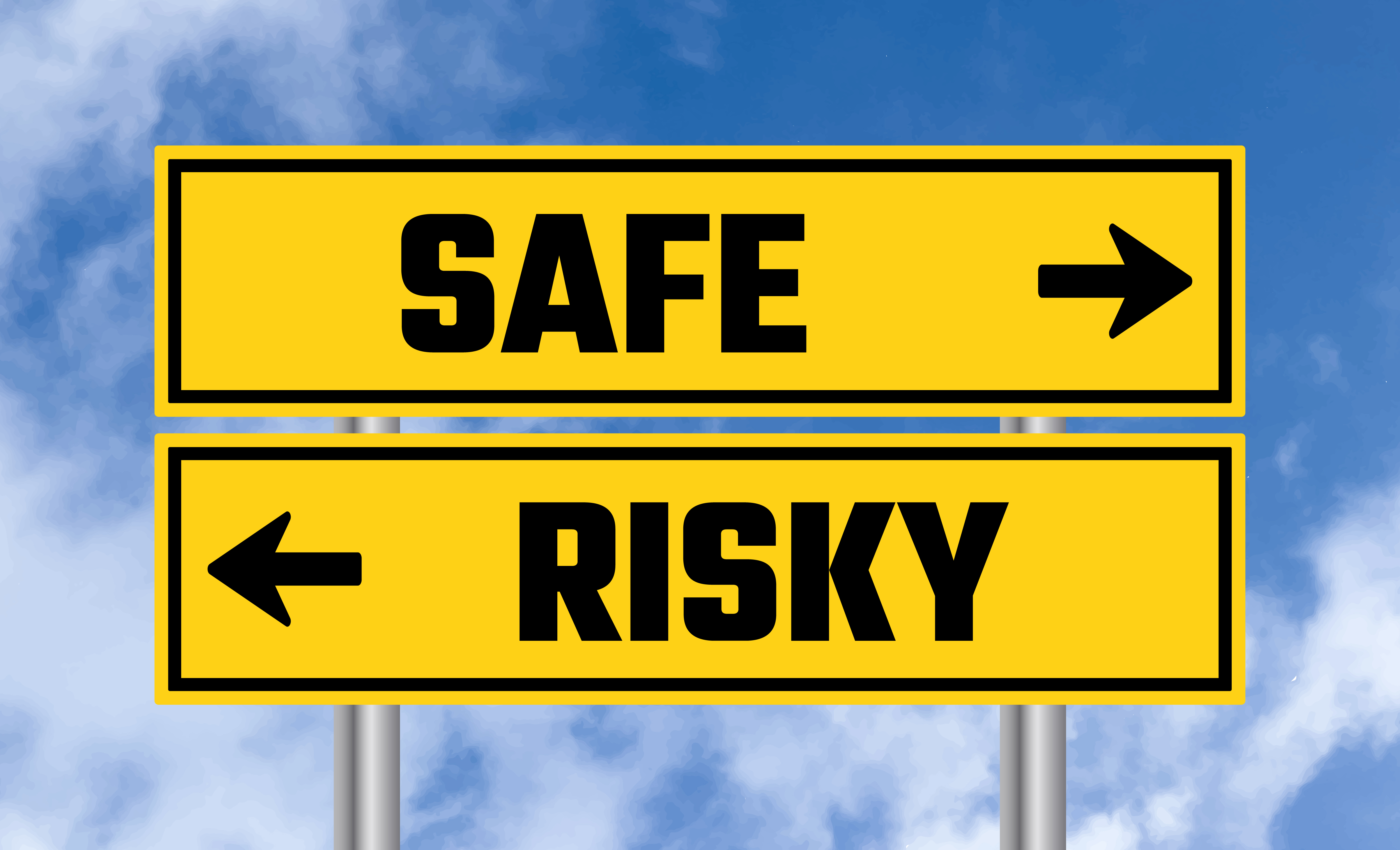 The image shows two yellow directional road signs against a blue sky with clouds. The upper sign points to the right and is labeled "SAFE," while the lower sign points to the left and is labeled "RISKY." This visual metaphor highlights the concept of decision-making, indicating the choice between a secure, presumably safer path and a more uncertain, possibly hazardous one. The intent is to emphasize the importance of awareness in selecting between different courses of action.